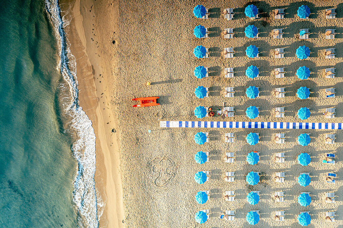 Sonnenschirme auf Sand, der von den Wellen des türkisfarbenen Meeres umspült wird, von oben, Vieste, Provinz Foggia, Gargano, Apulien, Italien