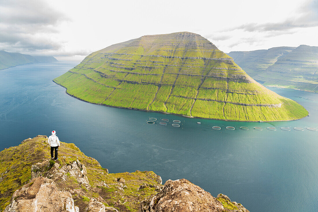 Hiker stands on top of a rock of Klakkur peak with Kunoy island in the background, Bordoy island, Faroe islands, Denmark, Europe