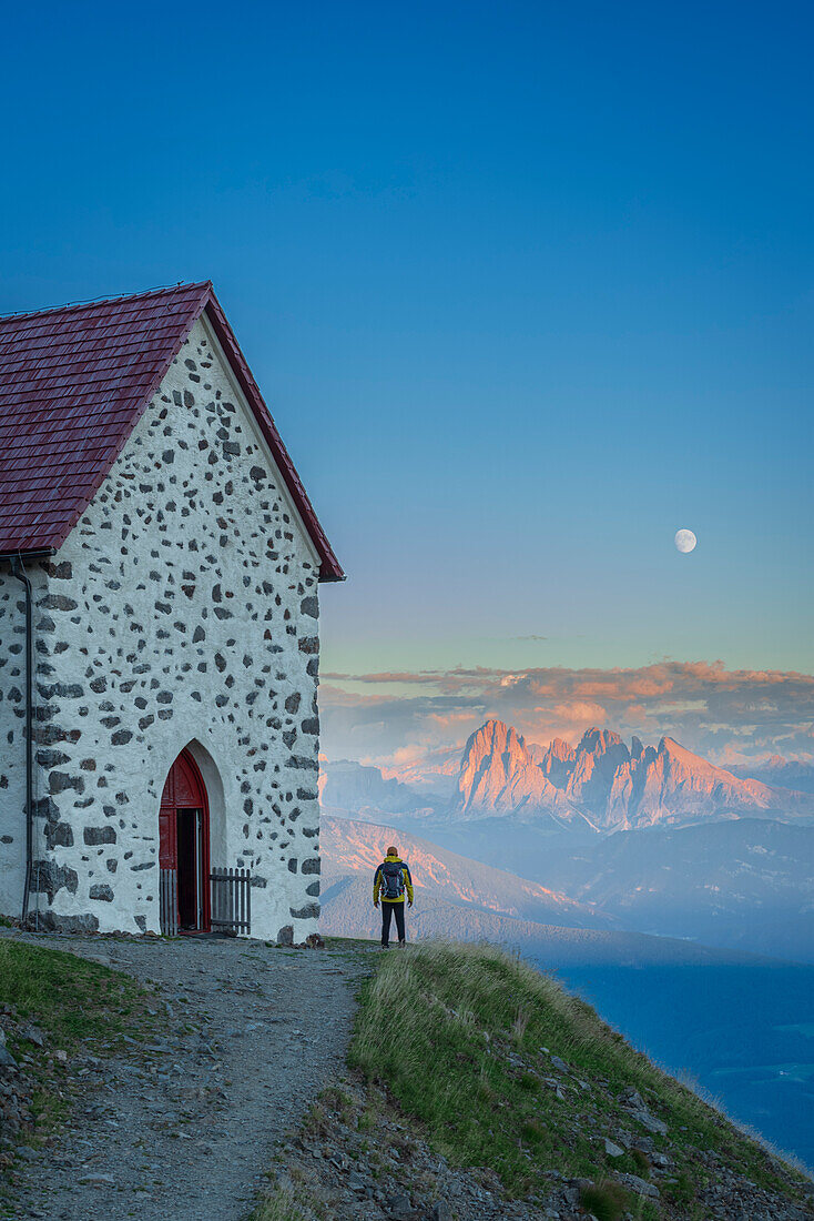 Rückenansicht eines Wanderers, der die Dolomiten vom Latzfonser Kreuz bei Sonnenuntergang und Vollmond bewundert, Lazfons, Klausen, Bezirk Bozen, Südtirol, Italien, Europa.
