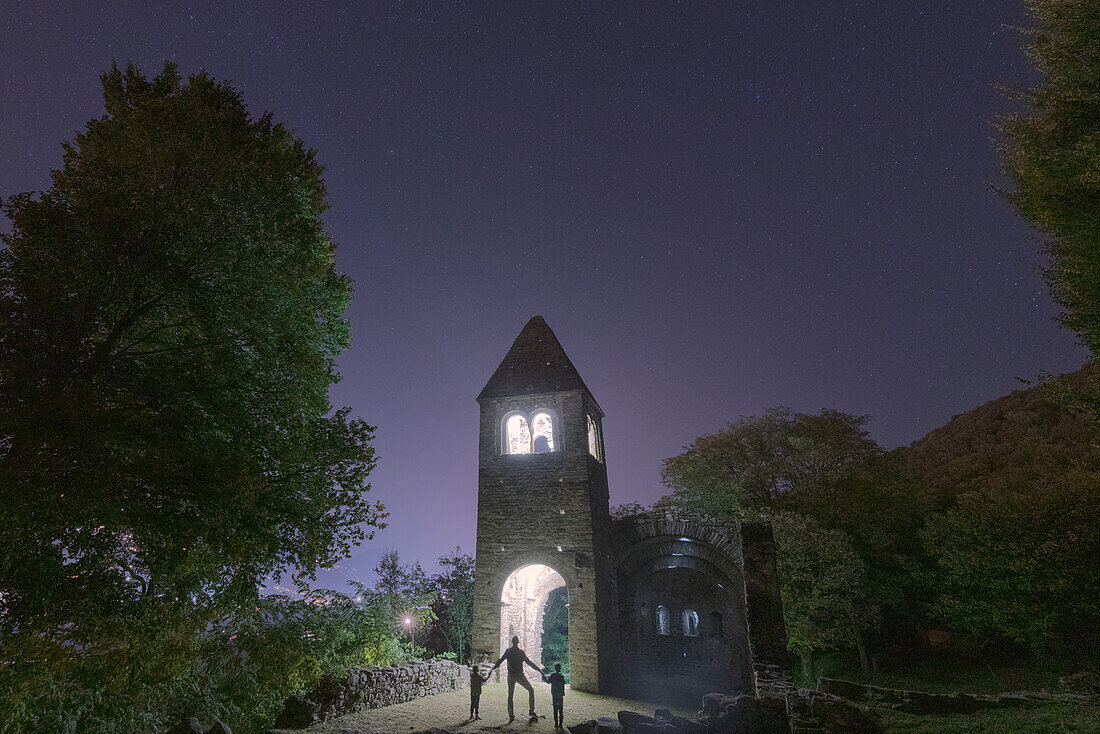 Cheerful man with two little boys sons admiring the illuminated abbey of San Pietro in Vallate, Valtellina, Lombardy, Italy