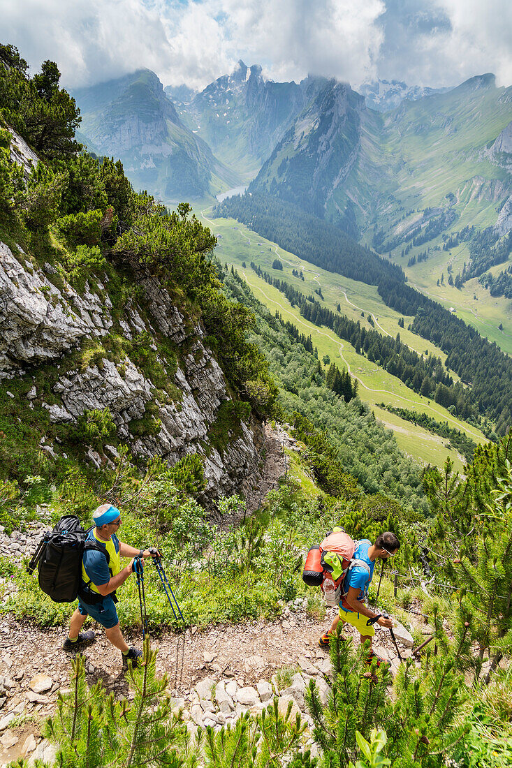Two hikers men with backpack walking on footpath on Saxer Lucke mountain, Appenzell Canton, Alpstein Range, Switzerland