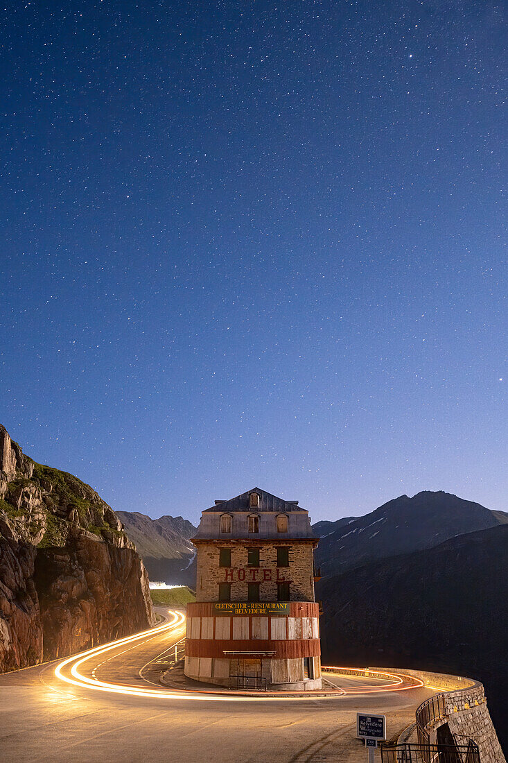 Sterne über Autospuren an den Haarnadelkurven der Furka-Passstraße und dem berühmten Hotel Belvedere, Kanton Wallis, Schweiz