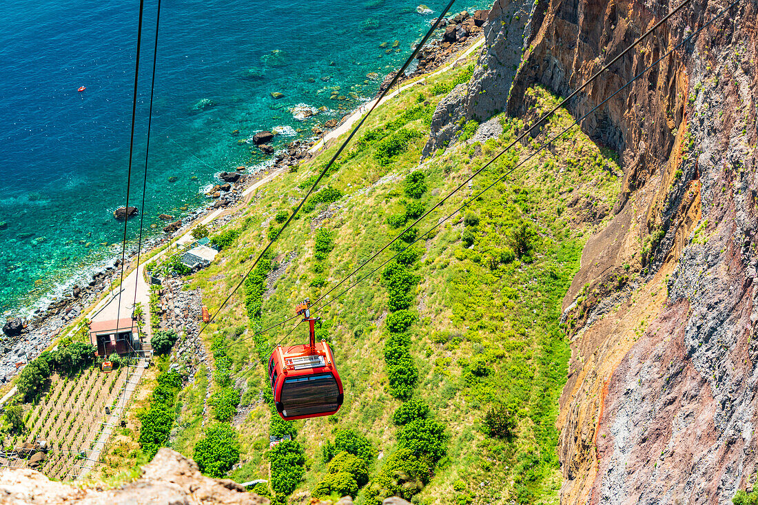 High angle view of scenic Teleferico Do Rancho cableway flying down to green fields oceanfront, Madeira island, Portugal