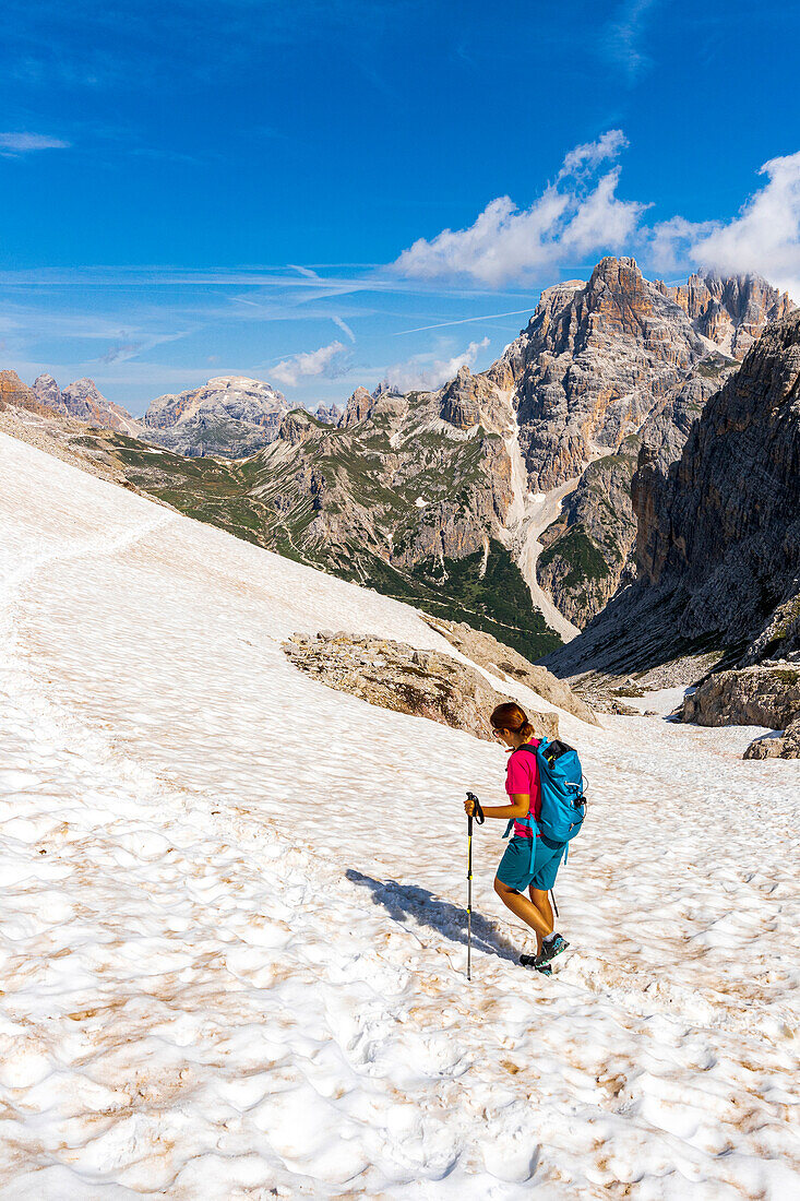 Woman with hiking poles walking in the snow on Forcella Dei Laghi mountain in summer, Sesto Dolomites, South Tyrol, Italy