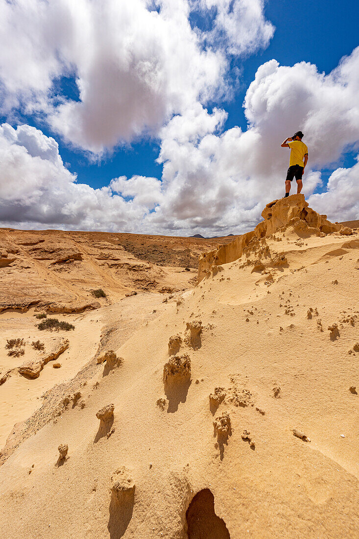 Wanderer, der die Aussicht genießt, während er auf einem Sandsteinfelsen steht, Barranco de los Encantados, Fuerteventura, Kanarische Inseln, Spanien