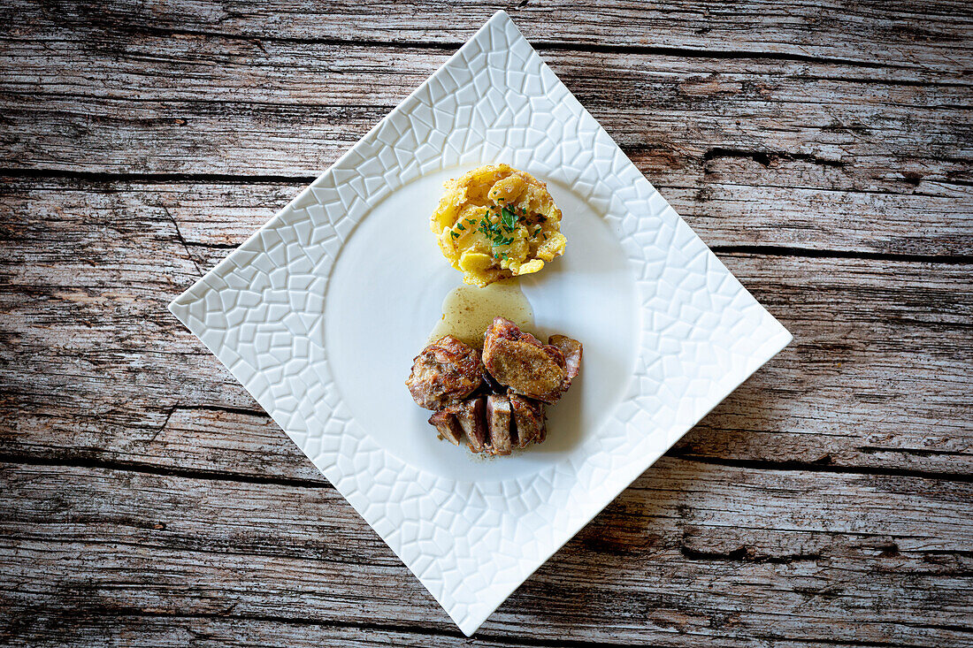 Sliced pork fillet with roasted potato in white plate on wood table background, Italy