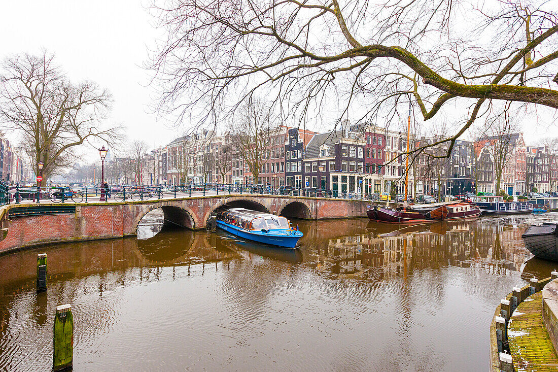 Fährboot während einer Grachtenfahrt unter der schmalen alten Brücke hindurch, Amsterdam, Nordholland, Niederlande
