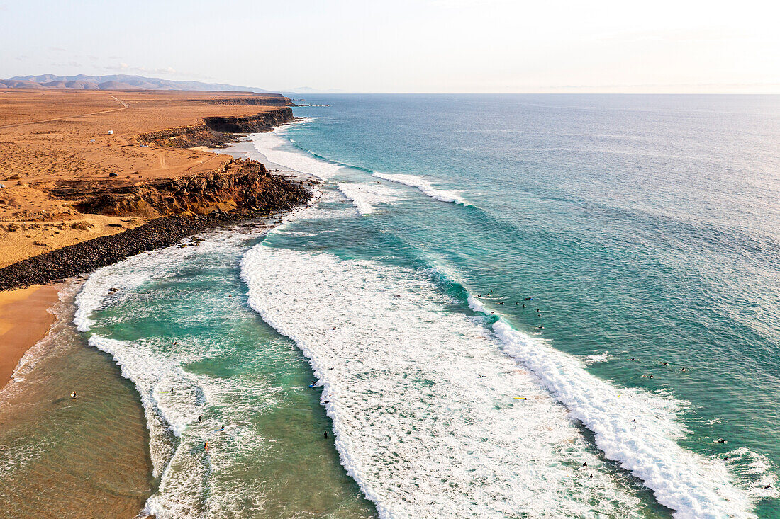 Luftaufnahme von Surfern, die am Strand von El Cotillo auf den Wellen des Ozeans reiten, Fuerteventura, Kanarische Inseln, Spanien