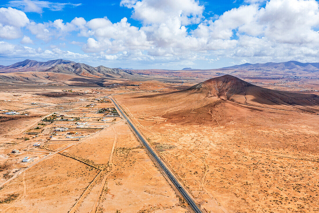 Luftaufnahme einer leeren, geraden Straße durch die vulkanische Berglandschaft, Tefia, Fuerteventura, Kanarische Inseln, Spanien