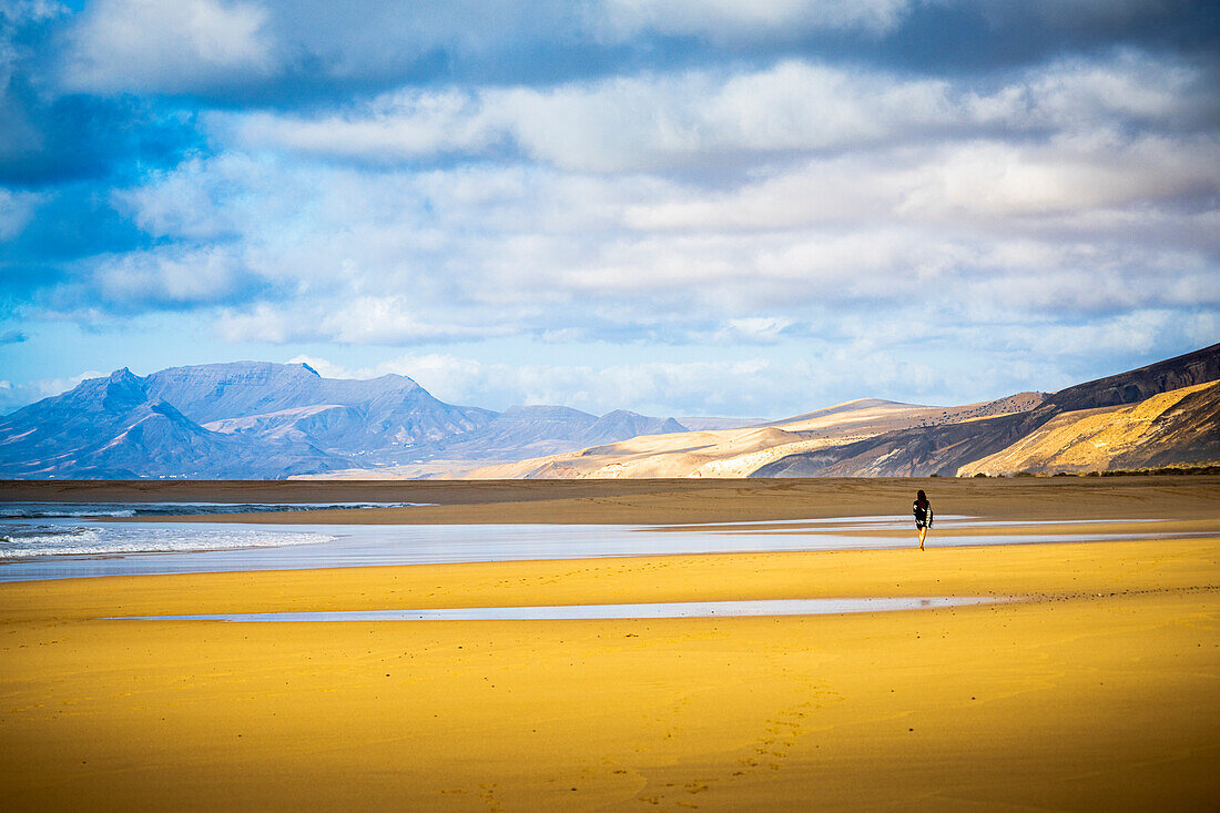 Young woman walking on the golden sand of Cofete Beach, Jandia natural park, Fuerteventura, Canary Islands, Spain