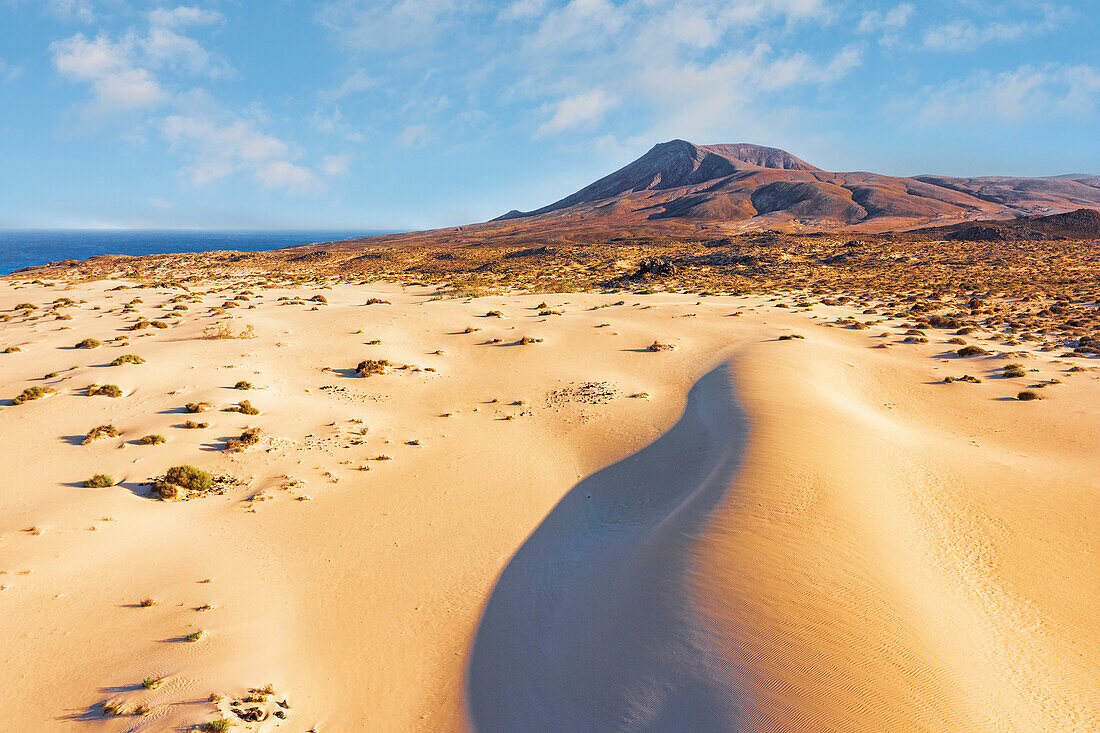 Wolken über roten Vulkanbergen und Sanddünen im Naturpark Corralejo, Fuerteventura, Kanarische Inseln, Spanien