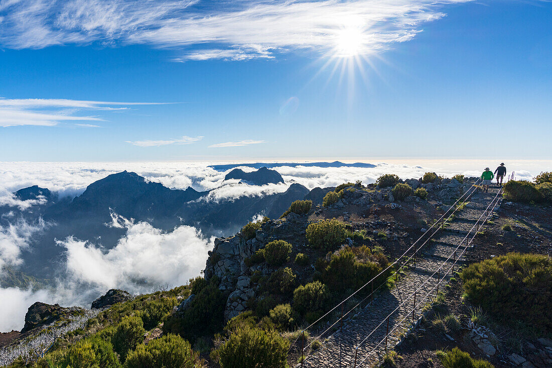 Hikers on path on Pico Ruivo mountain peak surrounded by clouds, Madeira, Portugal