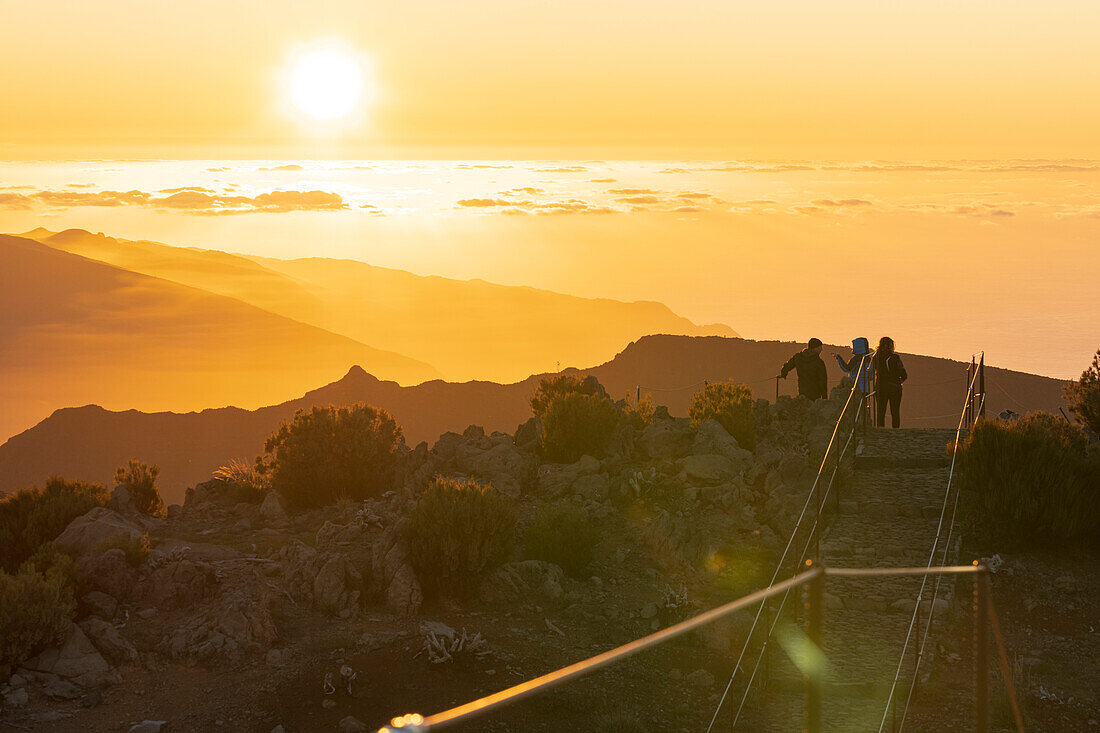 Drei Wanderer bewundern den Sonnenuntergang vom Gipfel des Pico Ruivo, dem höchsten Berg von Madeira, Portugal