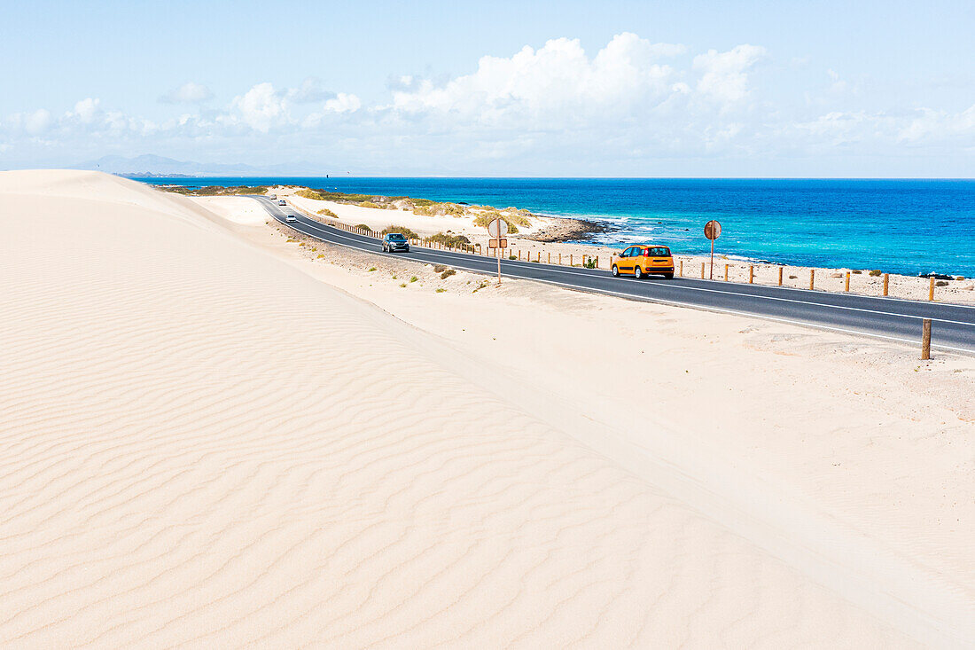 Car traveling on coastal road among sand dunes and ocean, Corralejo Natural Park, Fuerteventura, Canary Islands, Spain