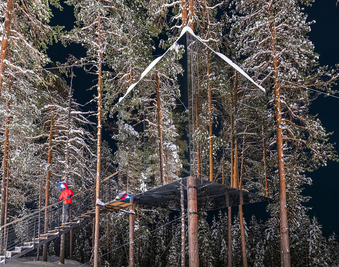 Hiker walking on steps leading to the cube shaped cottage with mirrors on the snowy trees, Tree hotel, Harads, Lapland, Sweden