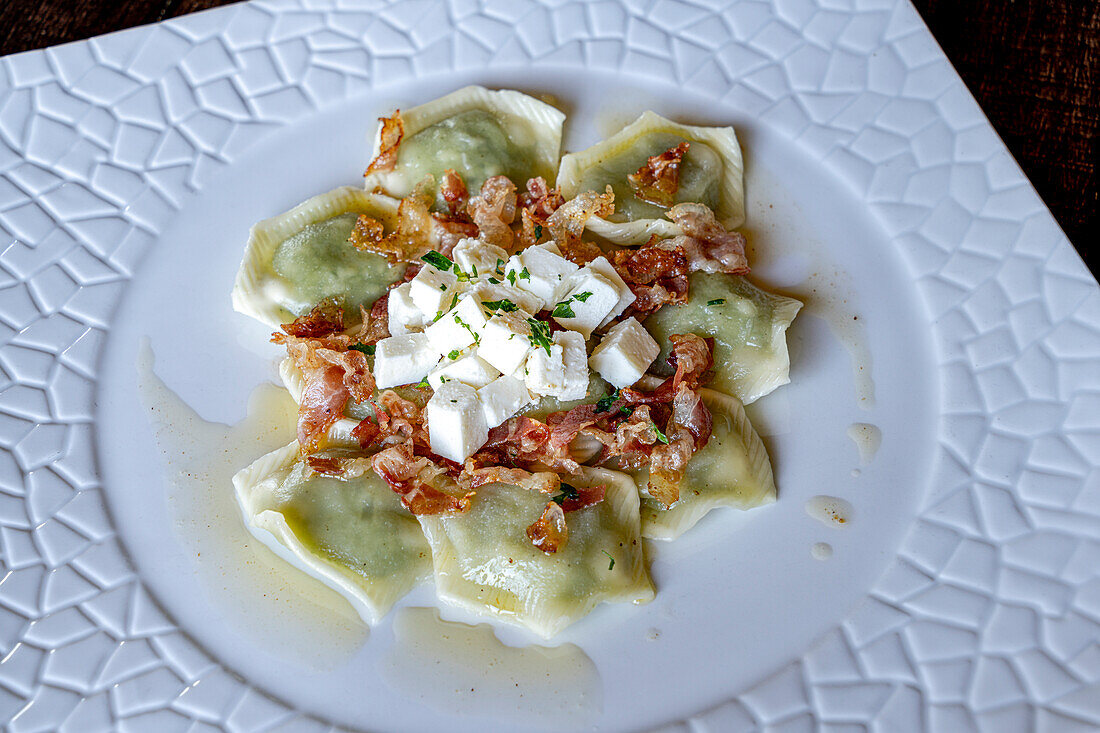 Mit Ricotta und Spinat gefüllte Ravioli, garniert mit gewürfeltem Ricotta und Speck, Italien