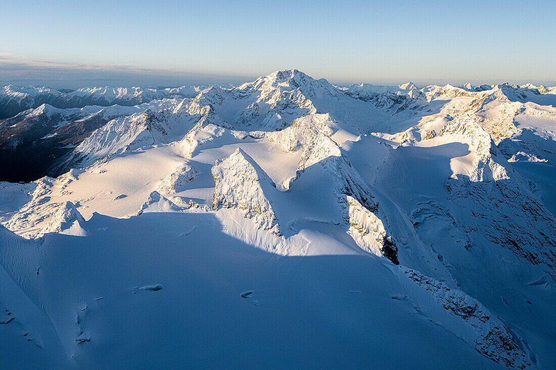 Winterliche Luftaufnahme des Pizzi del Sella und des Monte Disgrazia mit Schnee bedeckt bei Sonnenaufgang, Graubünden, Engadin, Schweiz