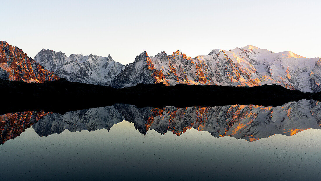 Silhouette einer Person, die den Sonnenuntergang über dem Mont-Blanc-Massiv beobachtet, das sich in den Lacs des Cheserys spiegelt, Chamonix, Hochsavoyen, Frankreich
