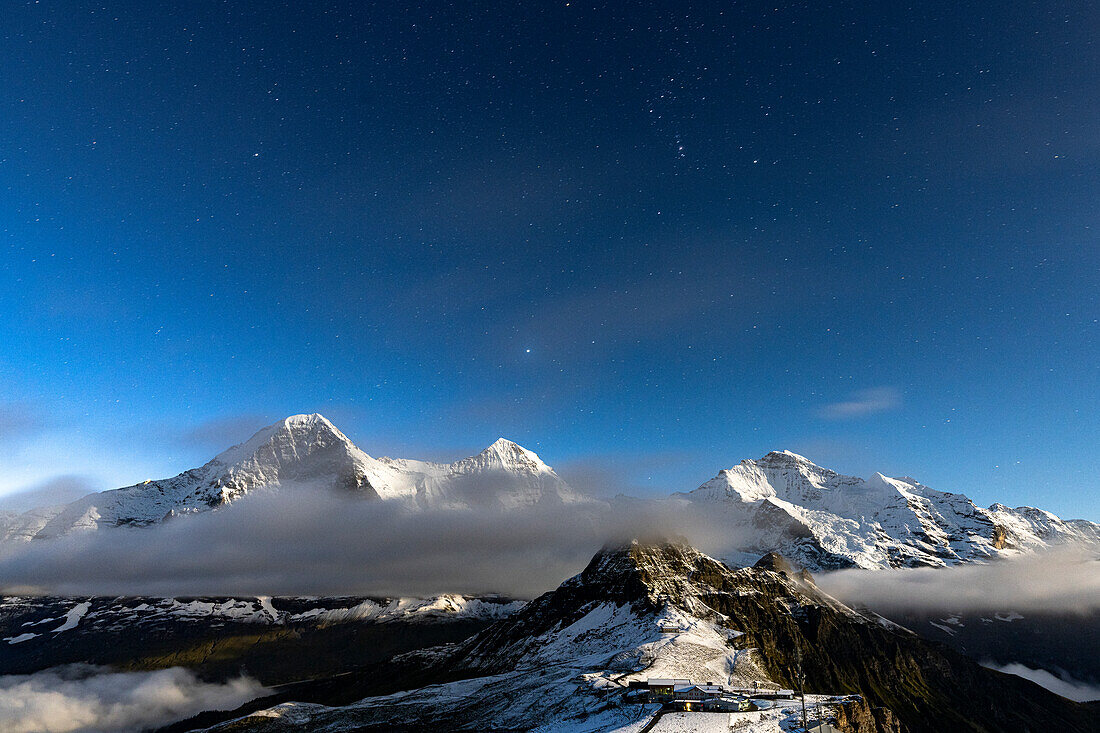 Nebel über den mit Schnee bedeckten Bergen Eiger, Mönch und Jungfrau unter dem Sternenhimmel, Mannlichen, Kanton Bern, Schweiz