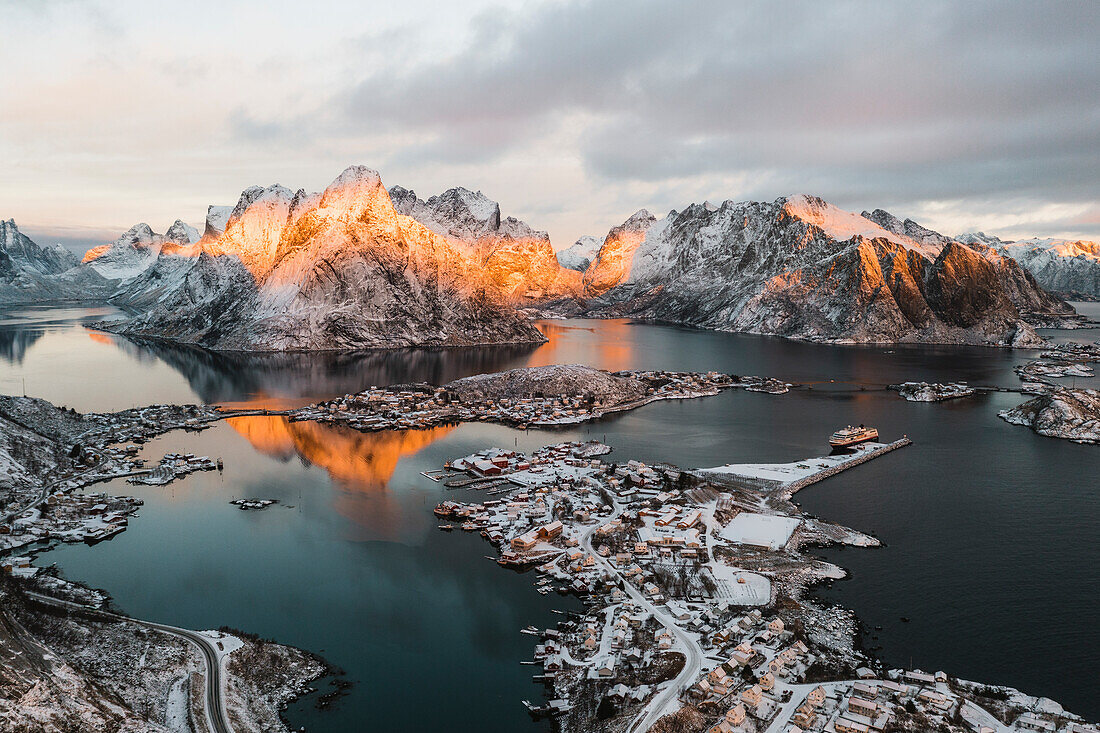 Winterlicher Sonnenaufgang über dem schneebedeckten Berg Olstind und der Bucht von Reine, Luftaufnahme, Reine, Nordland, Lofoten, Norwegen