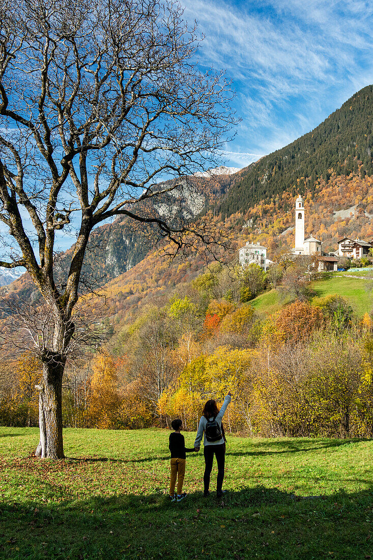 Rückansicht einer Mutter mit ihrem süßen Sohn, die das Alpendorf Soglio im Herbst bewundern, Kanton Graubünden, Schweiz