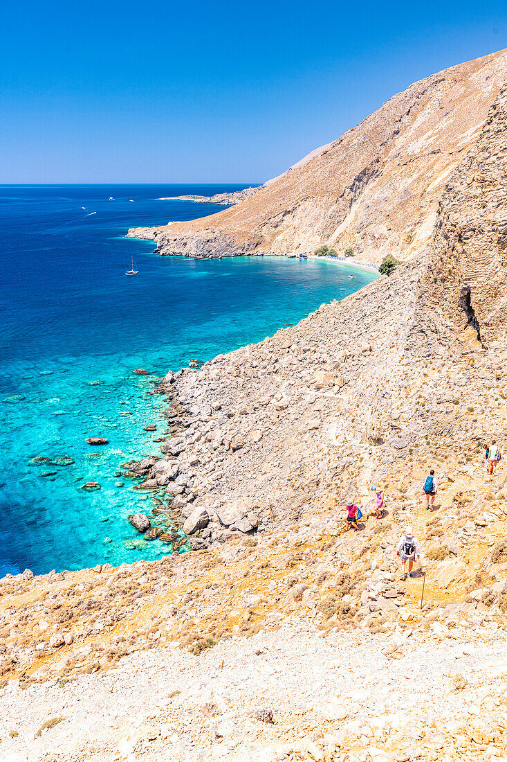 Hikers downhill on rocks towards the idyllic Glyka Nera beach in summer, Hora Sfakion, Crete island, Greece