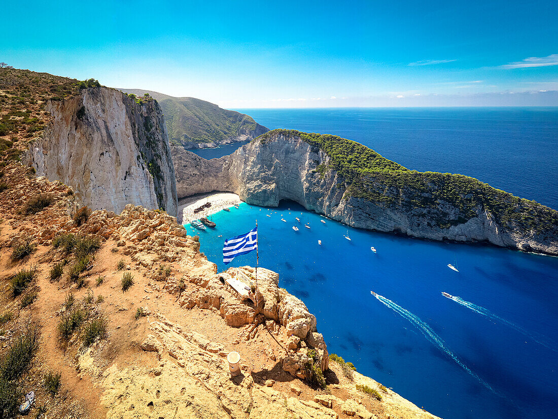 Griechische Flagge auf der Spitze majestätischer Klippen, Aussichtspunkt auf den berühmten Schiffswrack-Navagio-Strand, Zakynthos, Griechenland