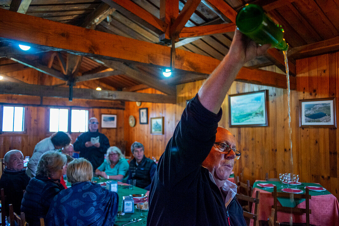 Ein spanischer Kellner gießt in einer Sideria im Restaurant El Casin in Picos de Europa, Parque Nacional de los Picos de Europa, Asturien, Kantabrien, Spanien, Europa, auf traditionelle Weise Apfelwein oder Sidra aus einer Flasche in ein Glas.