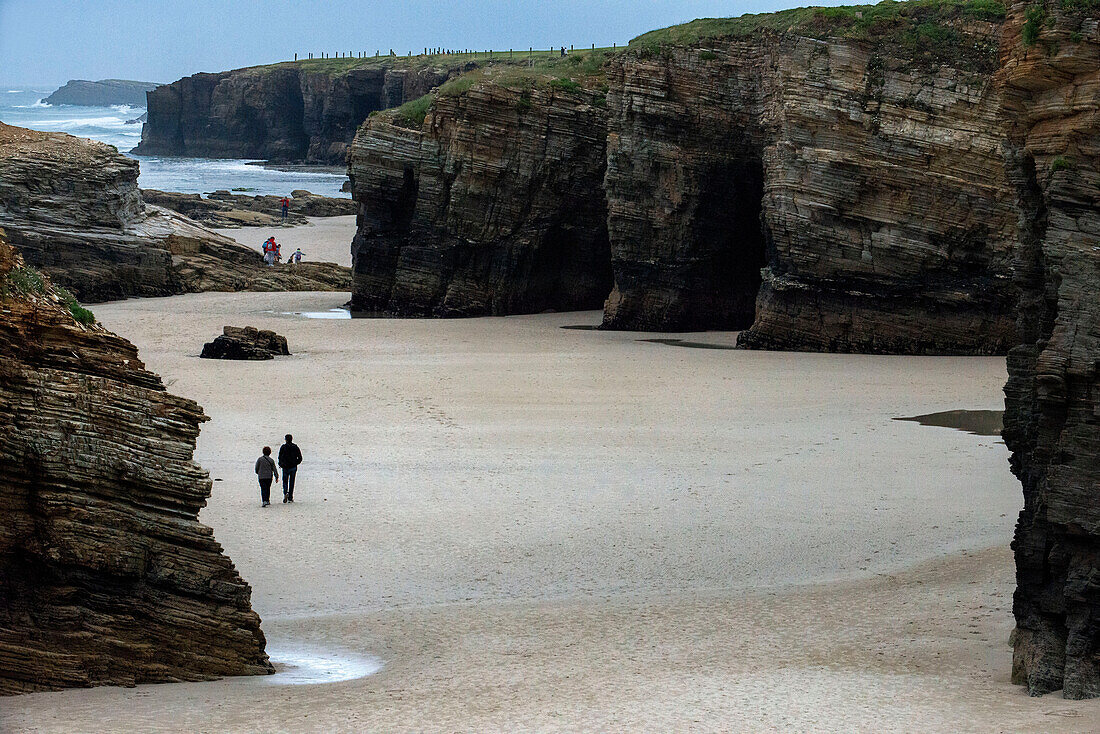 Der Strand von Catedrais oder Las Catedrales bei Sonnenuntergang, in Ribadeo, Lugo. Galicien, Spanien. Touristen bei einem Steinbogen am Strand des Naturdenkmals der Kathedralen in der Gemeinde Ribadeo, Provinz Lugo, Galicien, Spanien, Europa