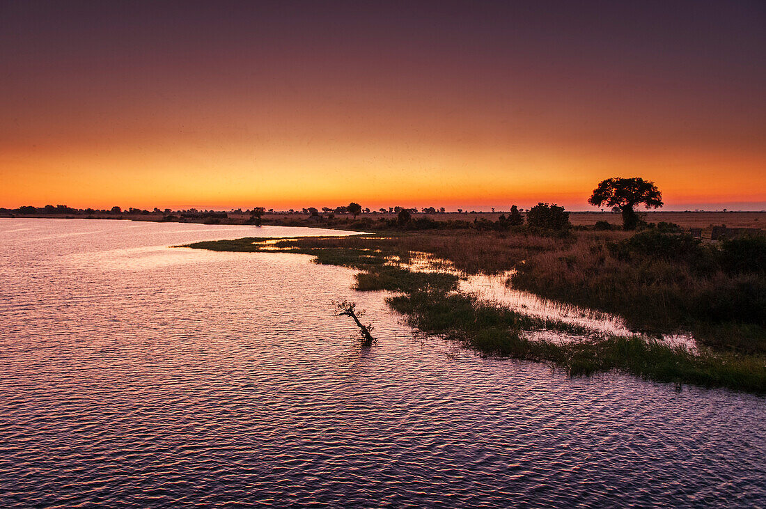 Der Chobe-Fluss und sein schemenhaftes Ufer bei Sonnenuntergang. Chobe-Fluss, Chobe-Nationalpark, Kasane, Botsuana.