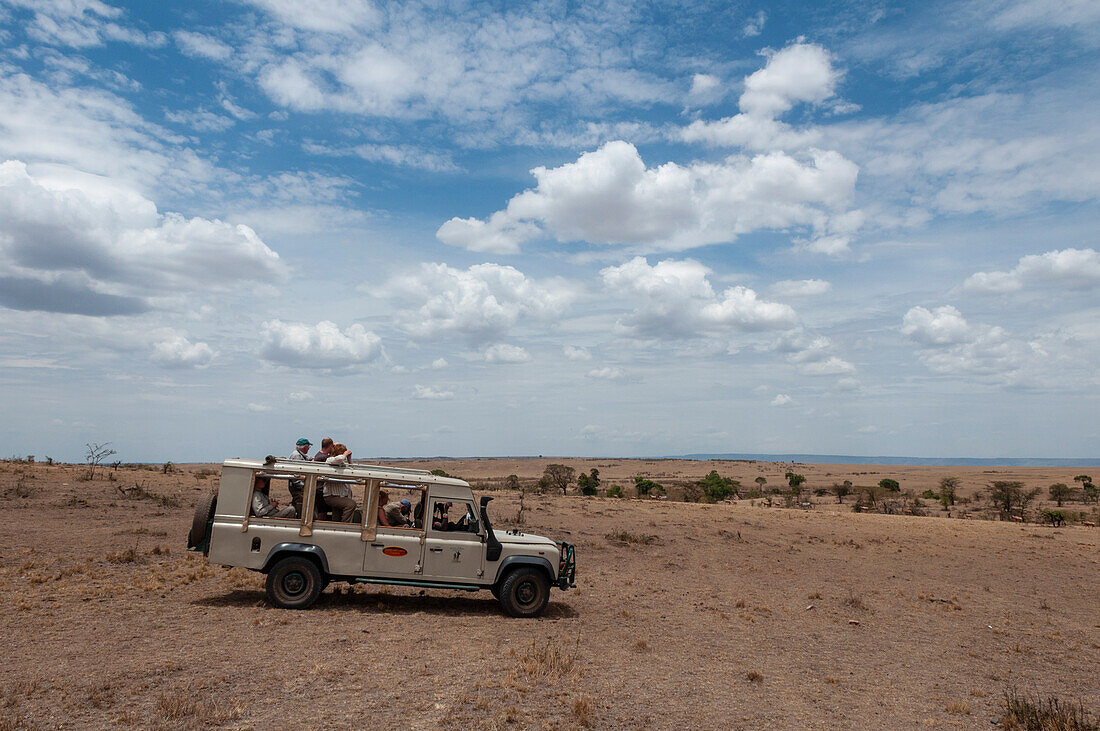 Ein mit Touristen gefülltes Safarifahrzeug in den weiten Ebenen des Masai Mara Nationalreservats. Masai Mara-Nationalreservat, Kenia.
