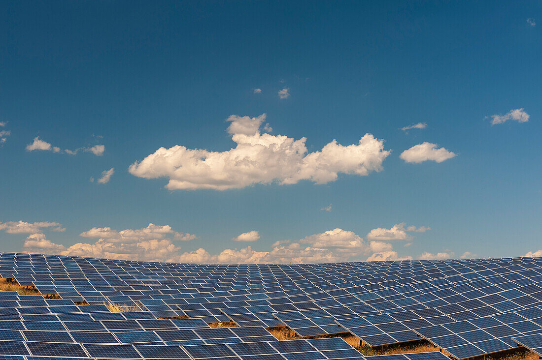 A field of solar panels at a solar power plant under a blue sky with puffy white clouds. Les Mees, Provence, France.