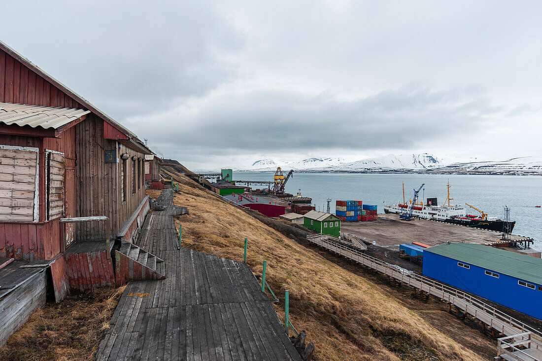 Gebäude, Ladedocks und Frachtschiffe an der Küste von Barentsburg. Barentsburg, Insel Spitzbergen, Svalbard, Norwegen.