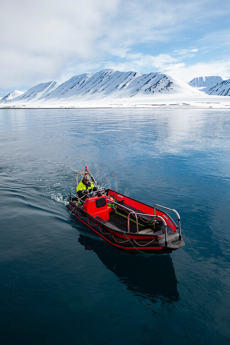 An inflatable raft cruises Mushamna Bay rimmed with mountains. Spitsbergen Island, Svalbard, Norway.