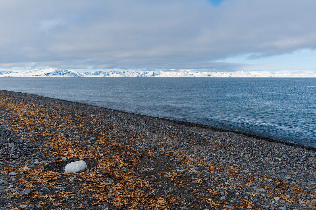 A rocky beach faces Mushamna Bay and snow covered mountains. Spitsbergen Island, Svalbard, Norway.