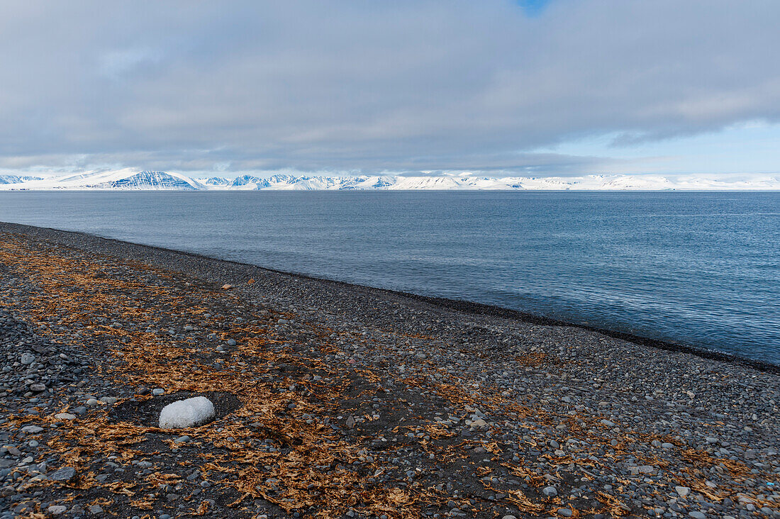 Ein felsiger Strand mit Blick auf die Mushamna-Bucht und schneebedeckte Berge. Insel Spitzbergen, Svalbard, Norwegen.