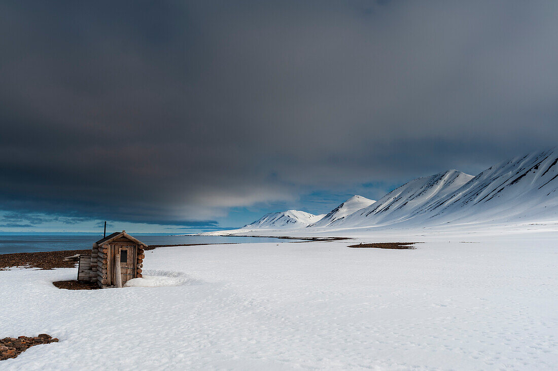 Eine Fuchsjagd-Blockhütte am schneebedeckten Strand von Mushamna. Mushamna, Insel Spitzbergen, Svalbard, Norwegen.