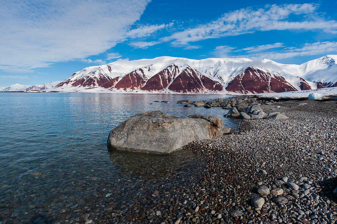 A gravel shoreline and snow covered mountains border Bockfjorden. Bockfjorden, Spitsbergen Island, Svalbard, Norway.