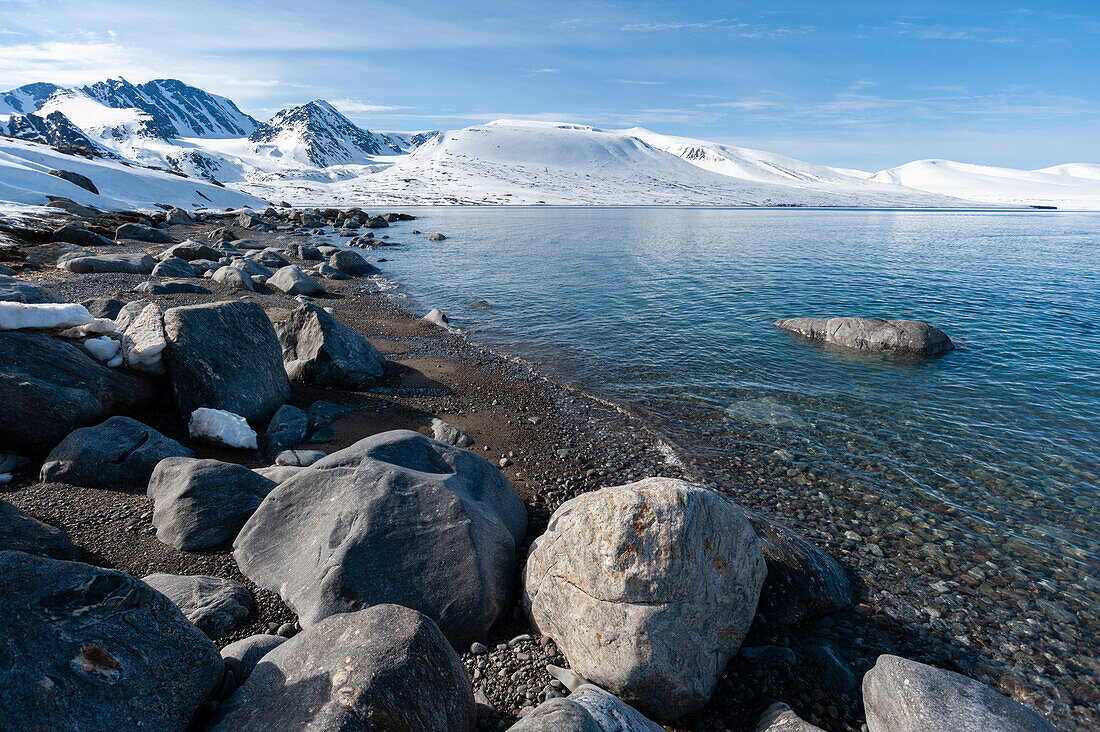 A rocky beach and snow covered mountains border Bockfjorden. Bockfjorden, Spitsbergen Island, Svalbard, Norway.