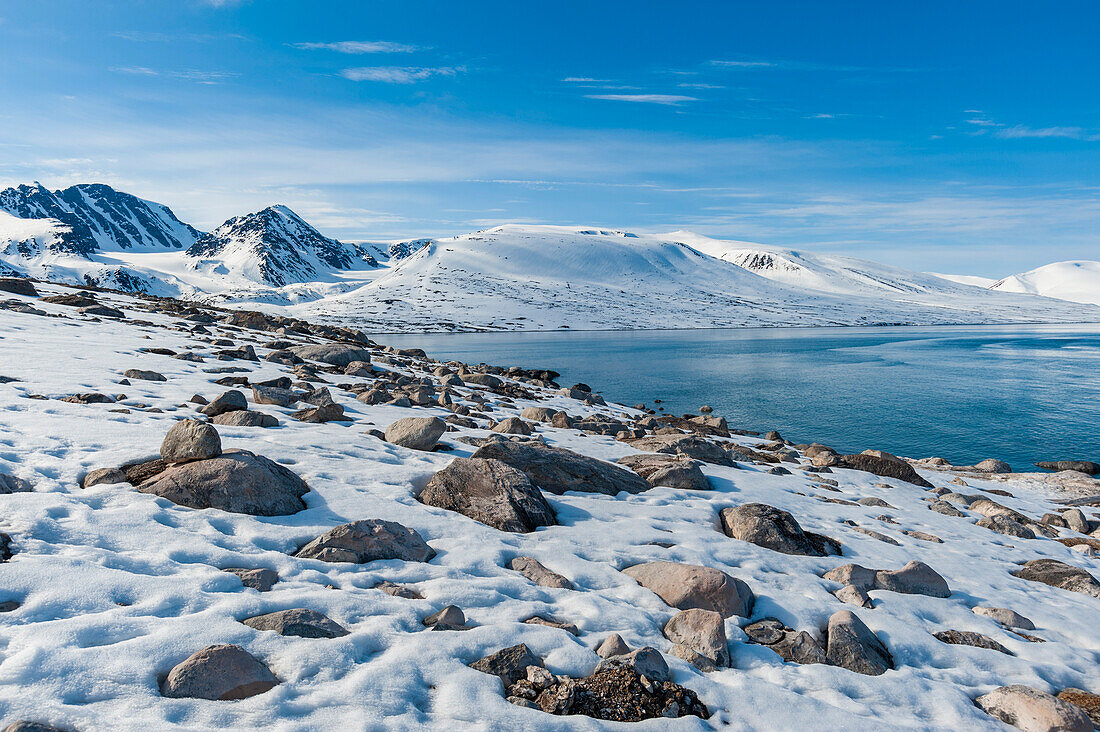 Snow covered rock beaches and mountains rim Bockfjorden. Bockfjorden, Spitsbergen Island, Svalbard, Norway.