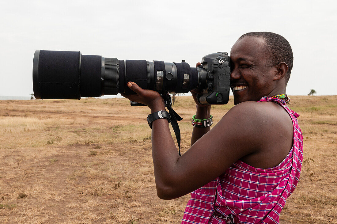 Saruni Kisemei, ein Masai-Führer, macht Fotos mit einem Teleobjektiv. Modell Freigegeben.