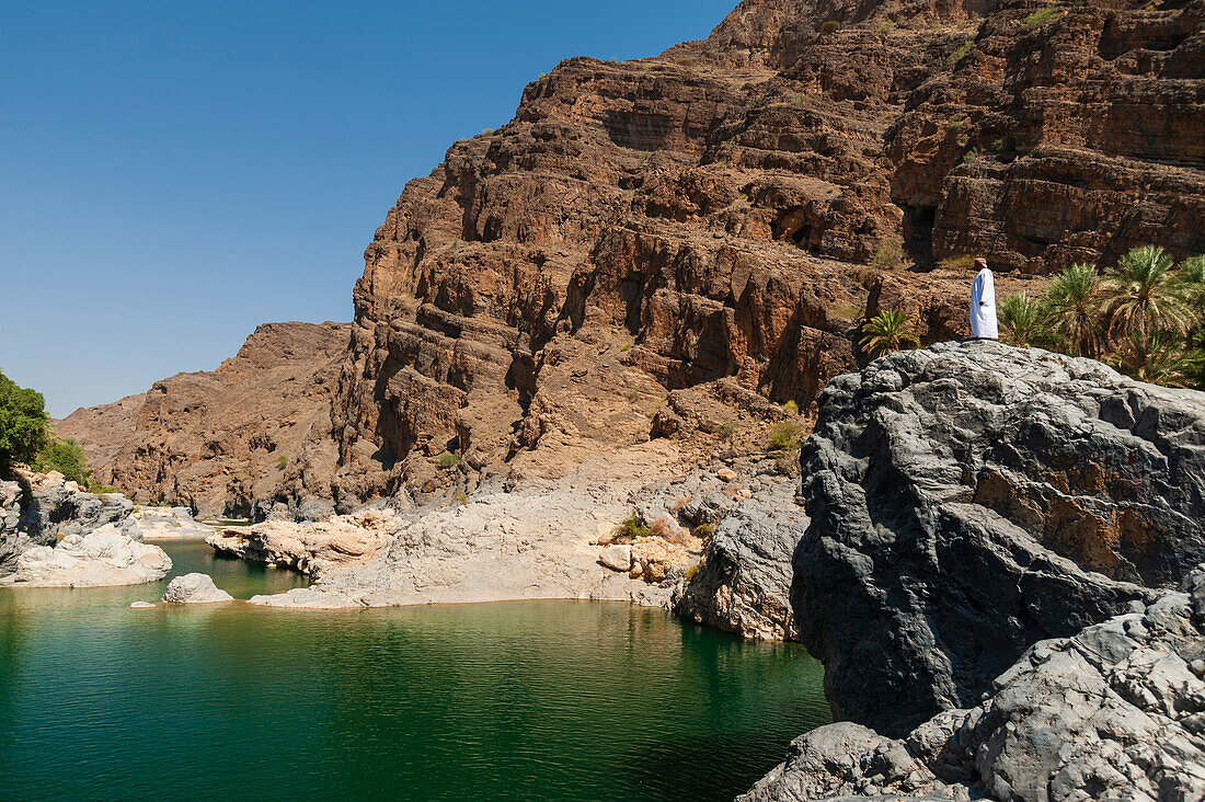 A man looking out over a natural pool in Wadi Al Arbeieen. Wadi Al Arbeieen, Oman.