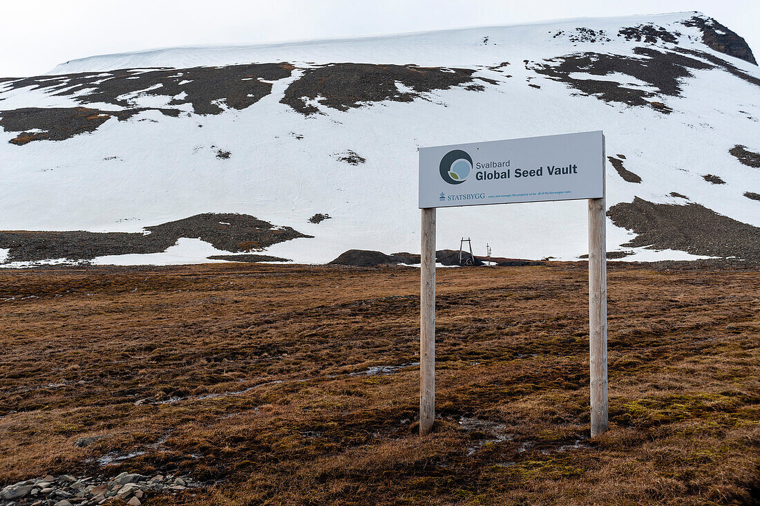 Ein Schild für den Svalbard Global Seed Vault in der Nähe eines schneebedeckten Berges. Longyearbyen, Insel Spitzbergen, Svalbard, Norwegen.