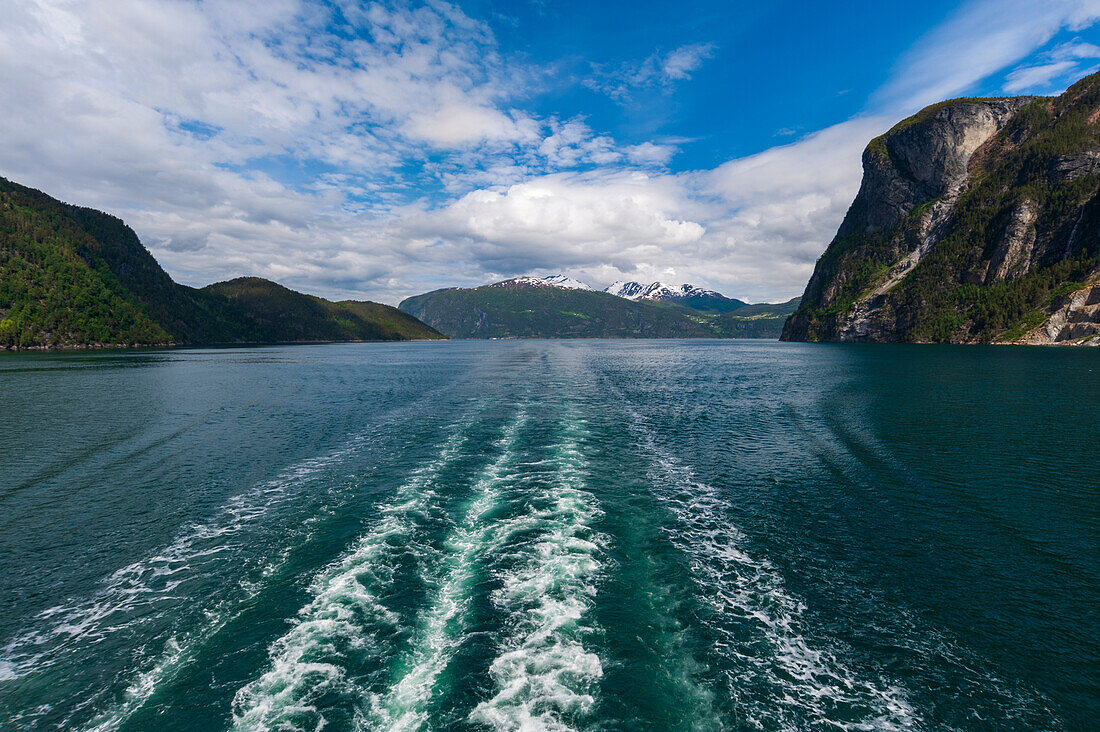 Das Kielwasser eines Schiffes zieht durch den Geirangerfjord, der von schroffen, steilen Bergen gesäumt wird. Geirangerfjord, Norwegen.