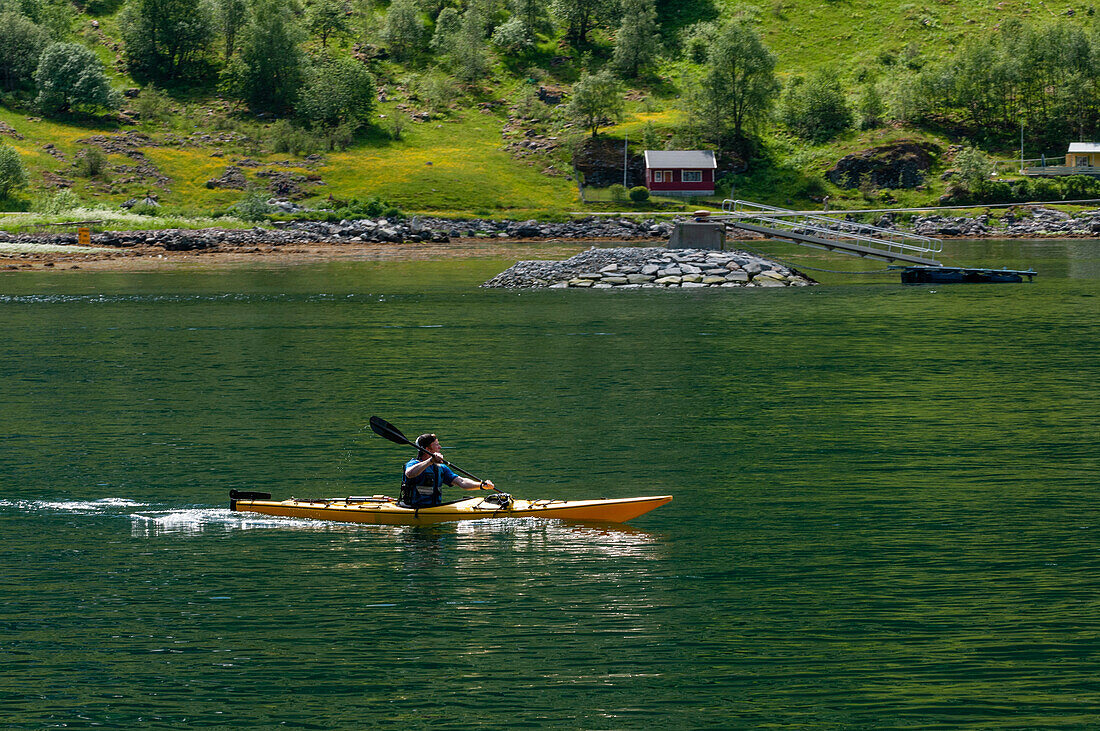 A kayaker paddles near a farm on the banks of Geirangerfjord. Geirangerfjord, Norway.