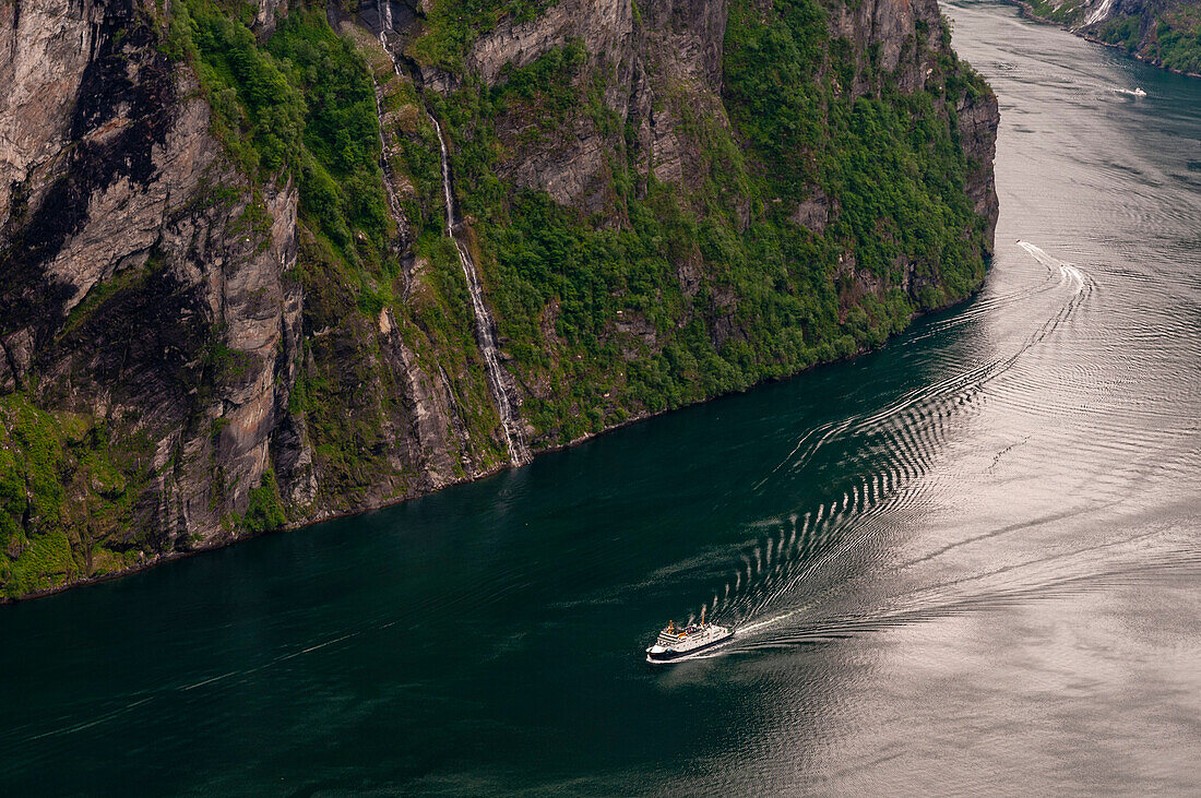A cruise ship navigates past sheer cliffs in Geirangerfjord. Geirangerfjord, Norway.