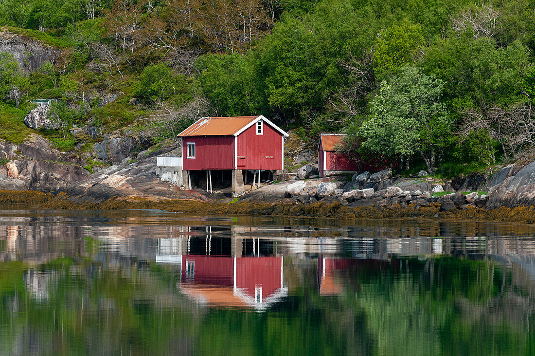 Ein hell gestrichenes Holzhaus spiegelt sich im Holandsfjord bei Svartisen. Svartisen, Holandsfjord, Norwegen.