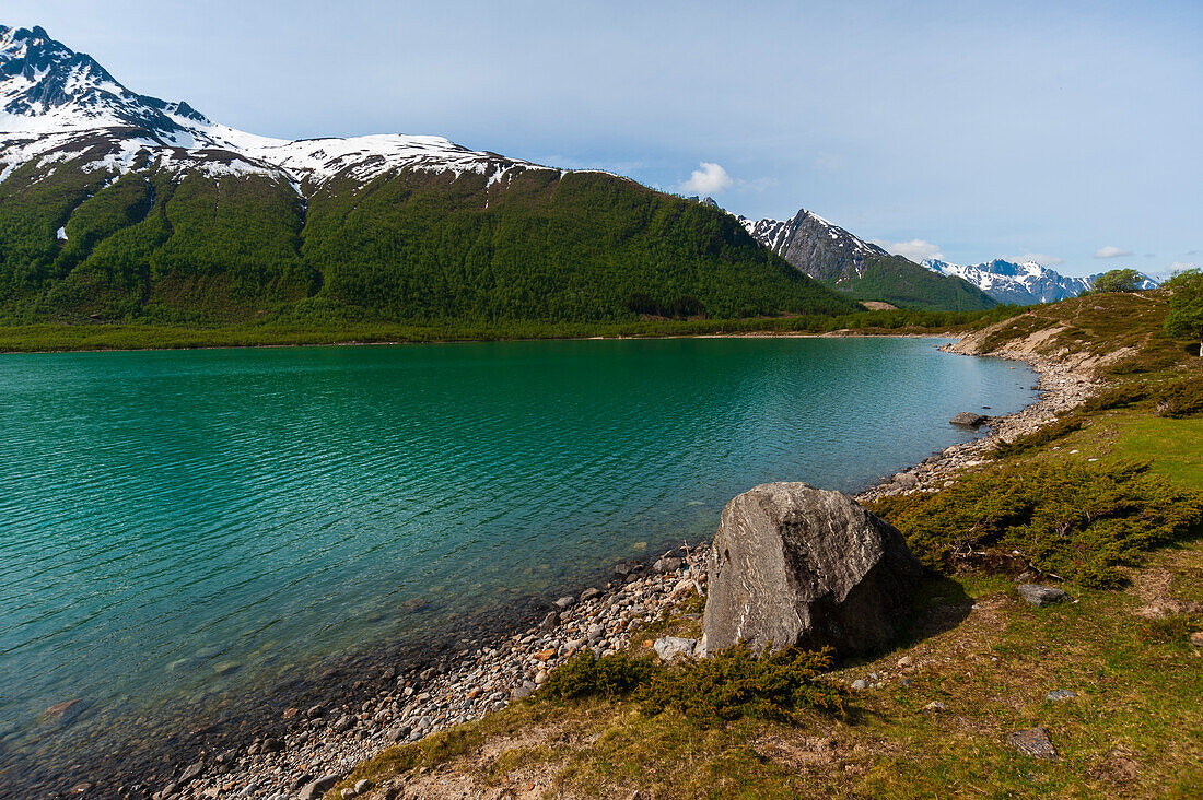 A glacial lake rimmed with ice streaked mountains and a gravel shoreline. Saltfjellet Svartisen National Park, Svartisen, Norway.