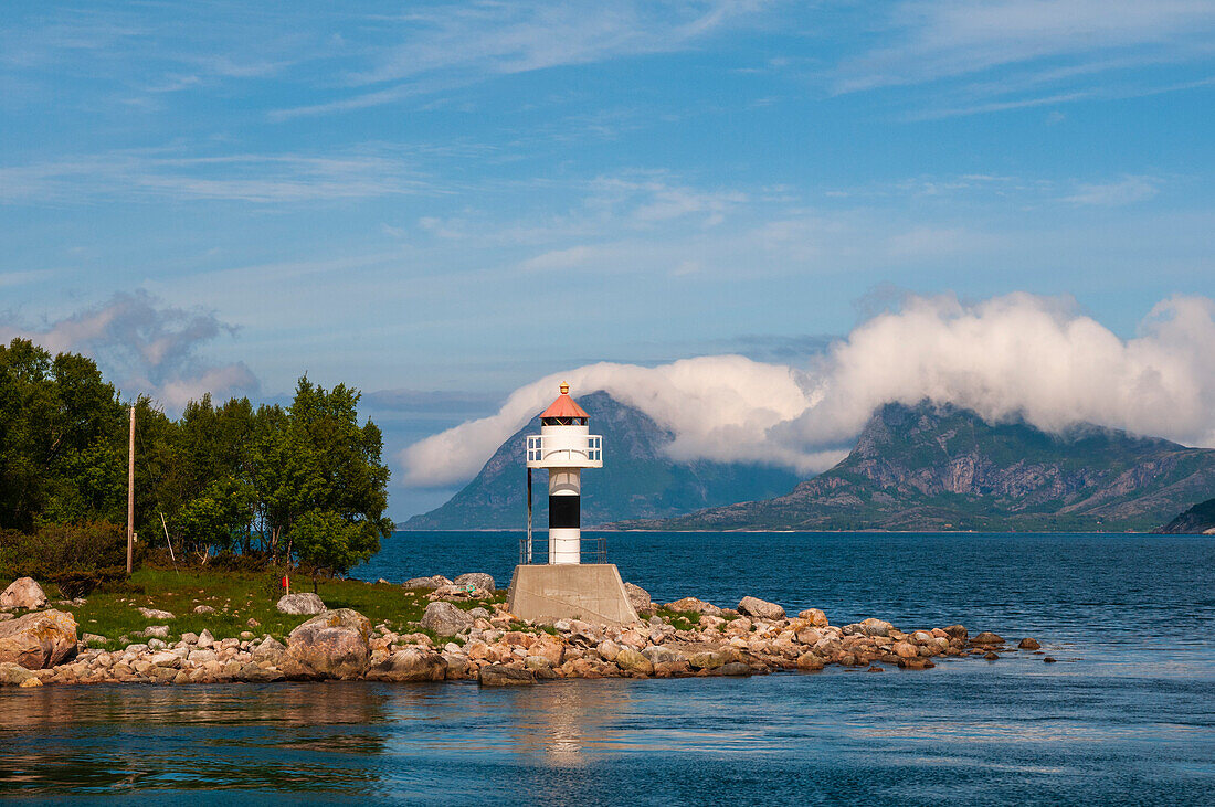 Ein Leuchtturm steht auf einem Felsvorsprung und spiegelt sich im Hollandsfjord. Svartisen, Norwegen.