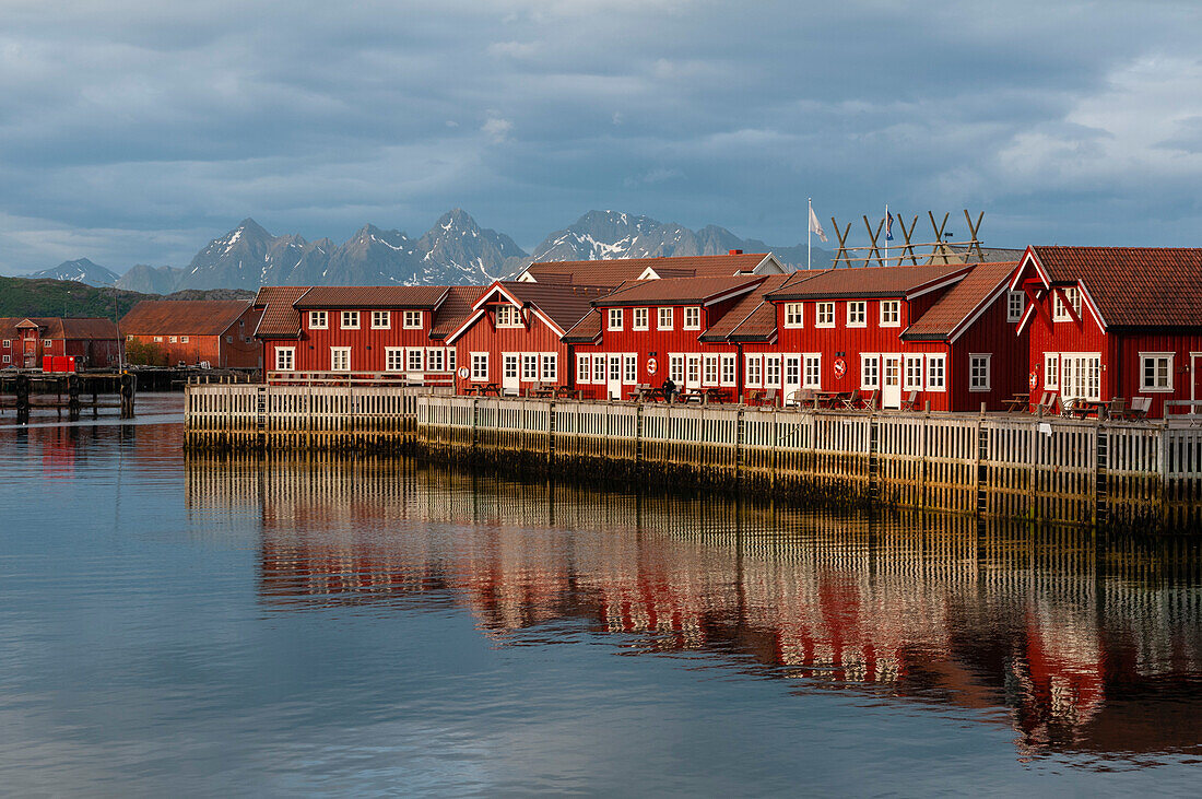 Hell gestrichene, sonnenbeschienene Häuser im Fischerdorf Svolvaer spiegeln sich im Wasser des Hafens. Svolvaer, Insel Austvagoya, Lofoten, Norwegen.